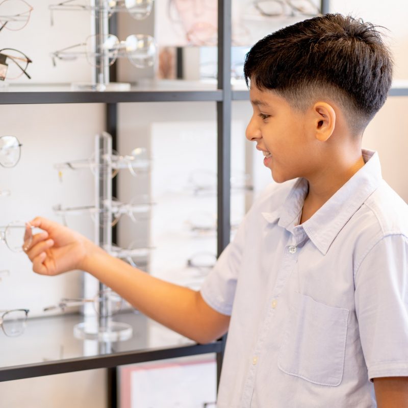 indian-boy-hold-glasses-on-shelf-during-selection-to-buy-some-products-for-his-eyecare.jpg